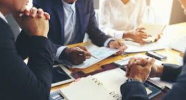 Group of business professionals in a meeting around a table, reviewing documents and taking notes.