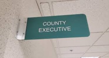 Green hanging ceiling sign that reads 'COUNTY EXECUTIVE'.